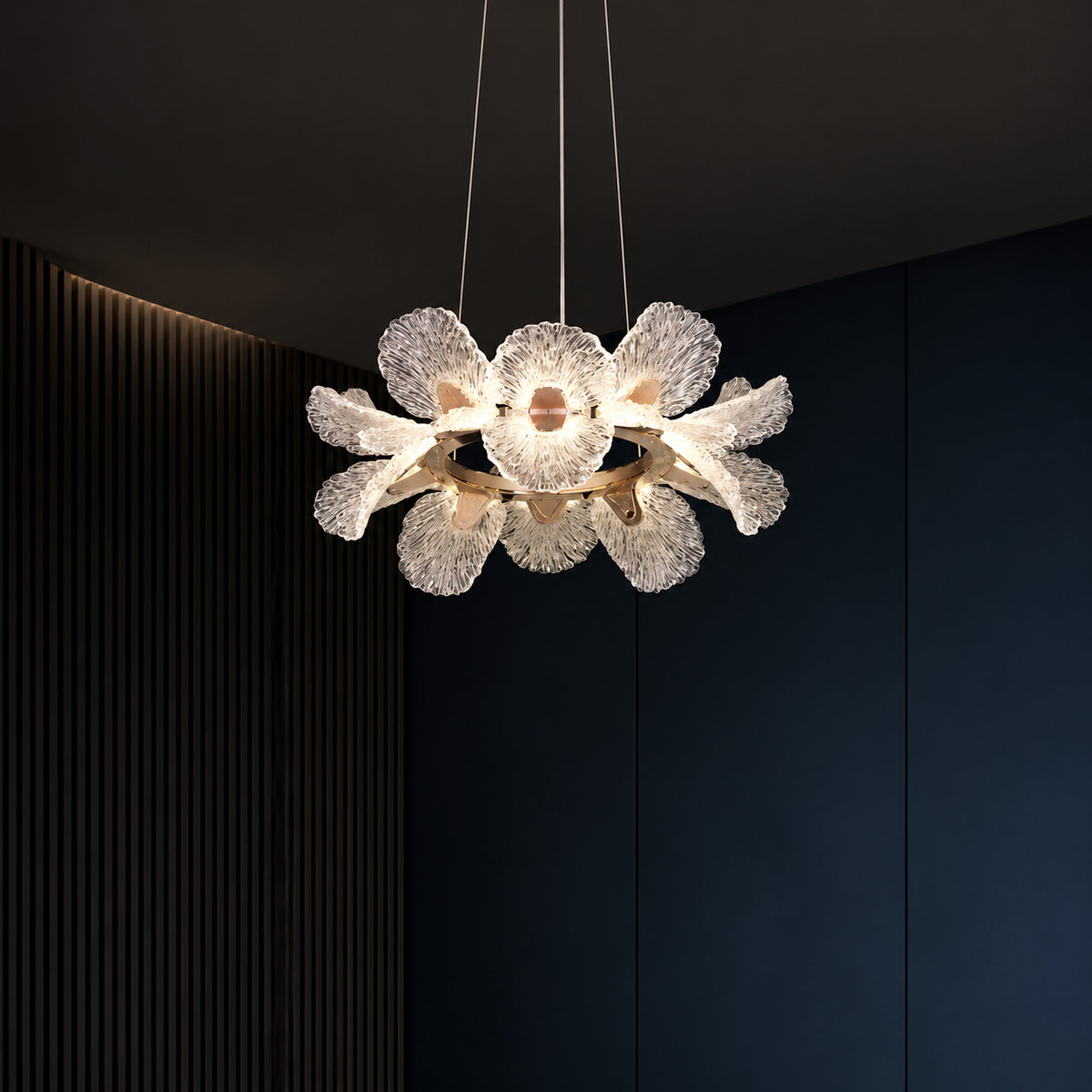 A modern flower-shaped pendant light with textured, translucent white petals and a warm glowing central bulb, suspended against a dark navy blue paneled wall.