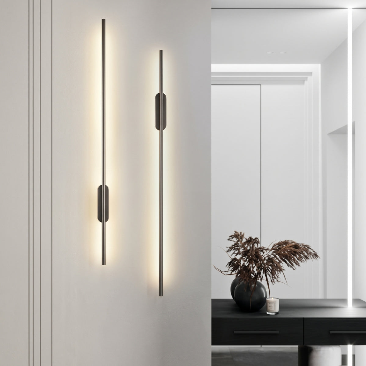Two thin, black vertical strip wall lights emitting a warm glow on a light grey wall in a modern room.