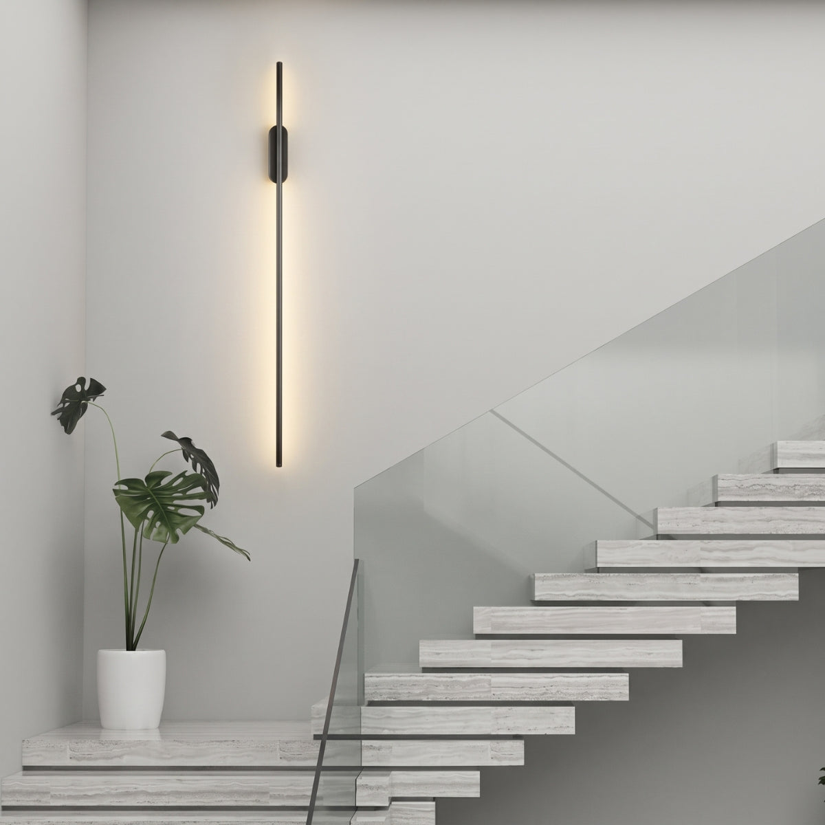 A long black vertical LED wall light mounted above a floating stone staircase with a glass railing.