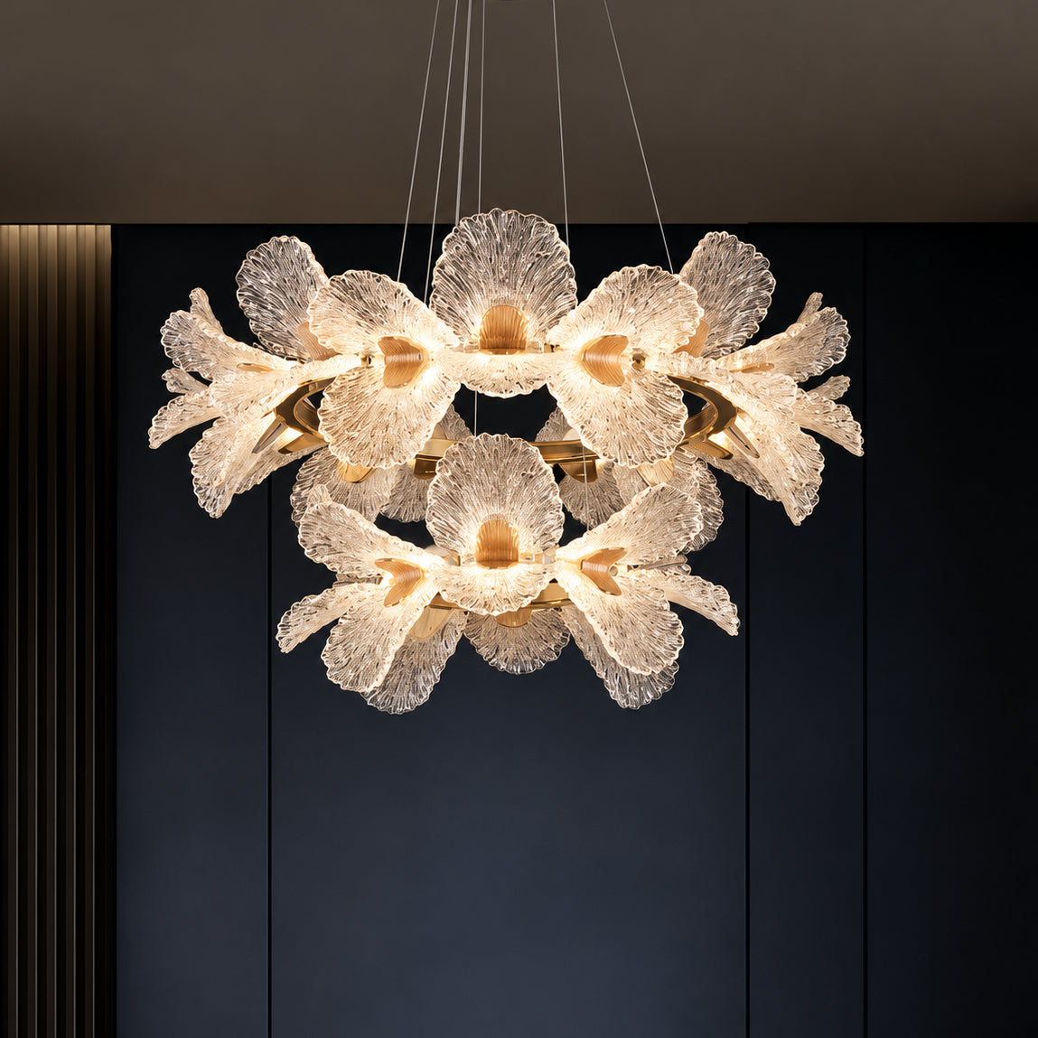 A modern multi-light chandelier with textured, flower-like glass shades suspended from a gold-toned ring, shown hanging against a dark paneled wall.