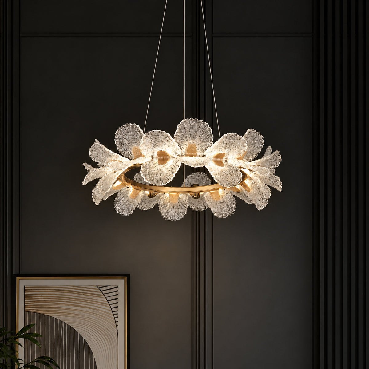 A modern floral ring pendant chandelier with textured, flower-like glass petals and a gold-toned circular frame, suspended against a dark paneled wall.